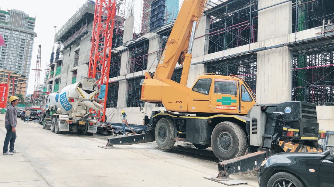 เครนล้อยาง CREVO 250 ทำงานที่ไซต์ก่อสร้างในเมือง มีรถโม่ปูน CPAC จอดข้างเคียง