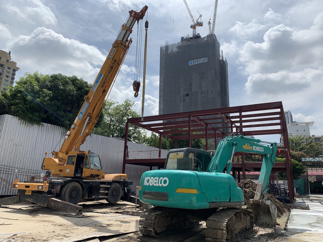 เครนล้อยาง KATO ของ BIG MACHINE TRADING ทำงานร่วมกับรถขุด KOBELCO ที่ไซต์ก่อสร้าง Cloud Residences SKV23 เห็นตึกสูงกำลังก่อสร้างด้านหลัง