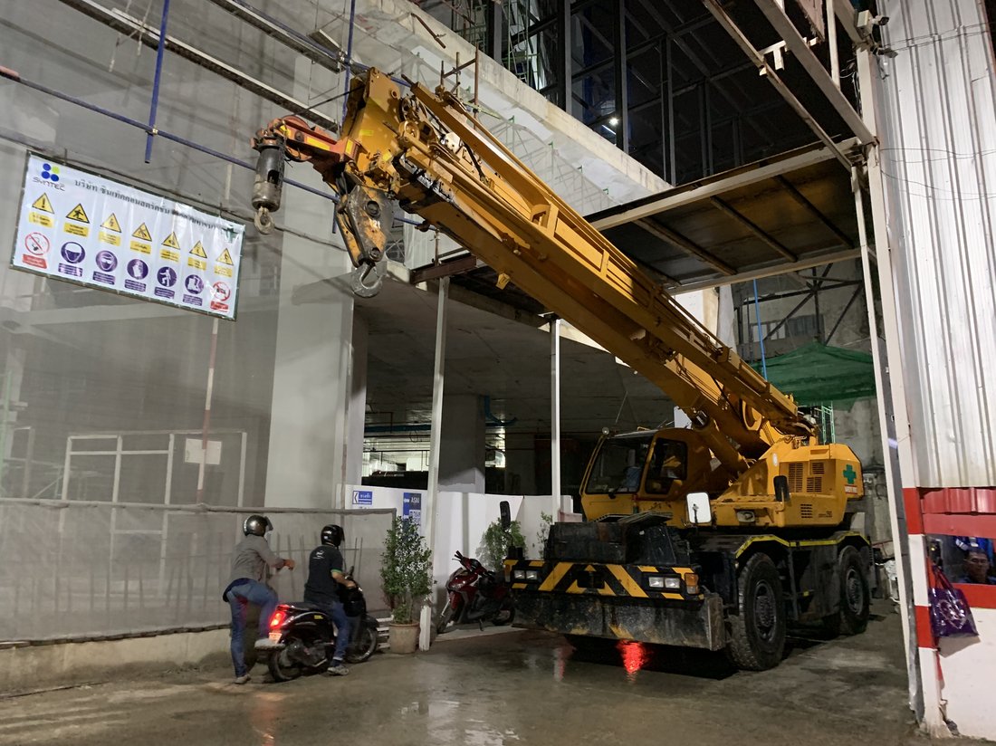 เครนล้อยาง BIG MACHINE TRADING ทำงานกลางคืนที่ไซต์ก่อสร้าง I'm Chinatown มีคนขี่มอเตอร์ไซค์ผ่านหน้างาน
