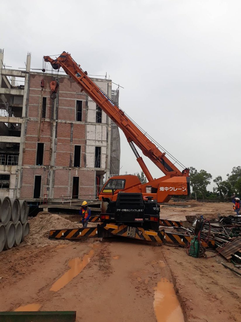เครนล้อยาง BIG MACHINE TRADING ยกของขึ้นอาคารวิทยาลัยเทคโนโลยีไออาร์พีซี มีทีมงานสวมเสื้อสะท้อนแสงดูแลหน้างาน