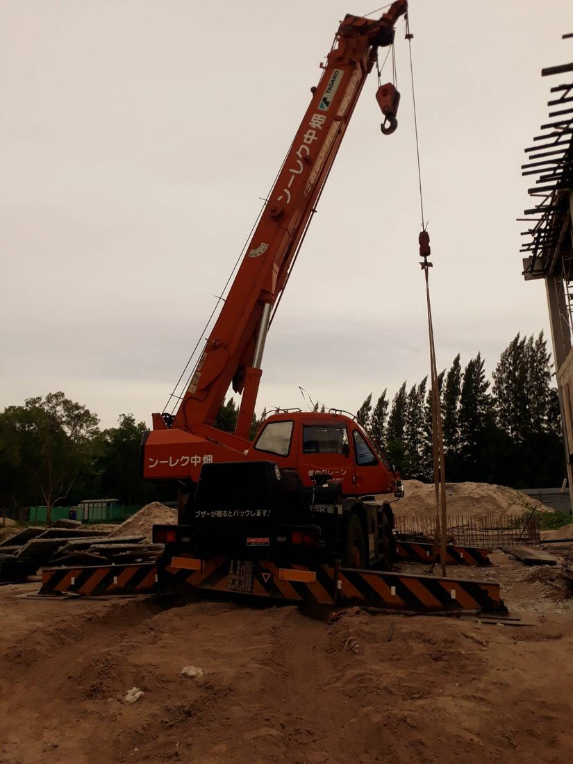 เครนล้อยาง BIG MACHINE TRADING ตั้งขาค้ำยันพร้อมยกของขึ้นสูง ที่ไซต์ก่อสร้างวิทยาลัยเทคโนโลยีไออาร์พีซีช่วงพลบค่ำ