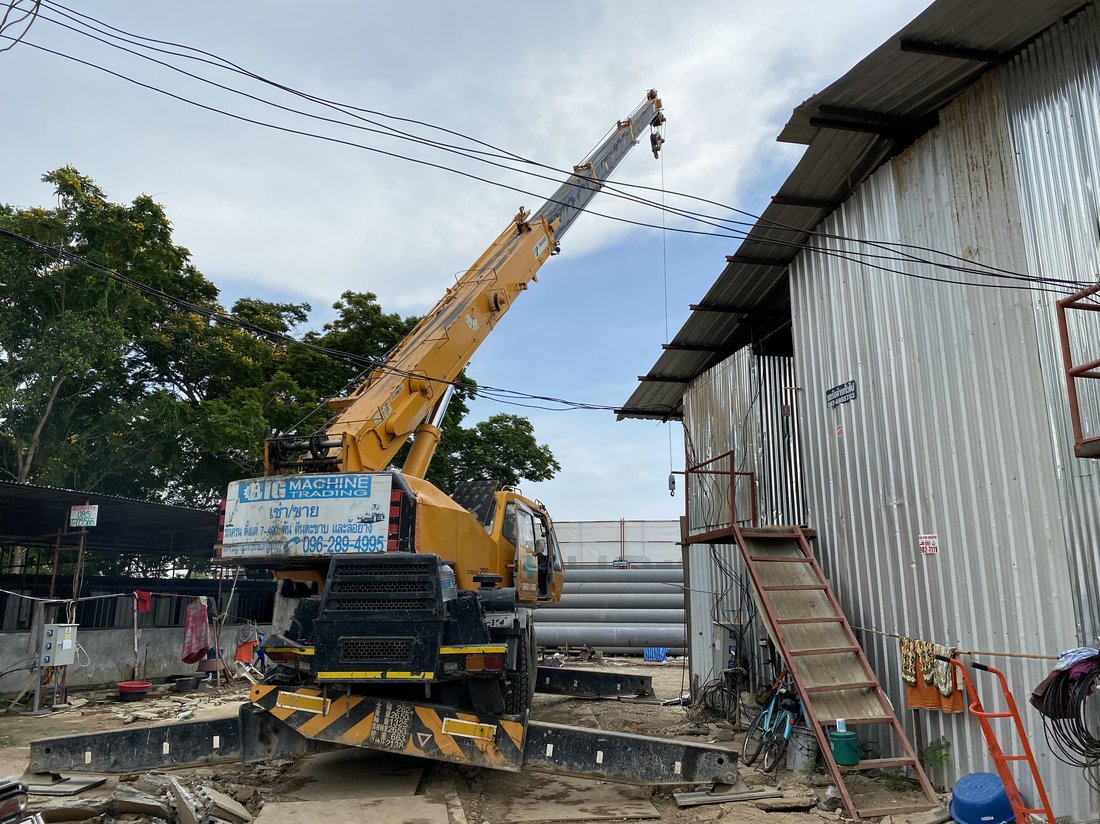 เครนล้อยาง BIG MACHINE TRADING ยกของขึ้นอาคารเก่าที่ไซต์ก่อสร้างกองกำกับการ 1 กองบังคับการตำรวจน้ำ เห็นป้ายบริษัทติดท้ายเครน