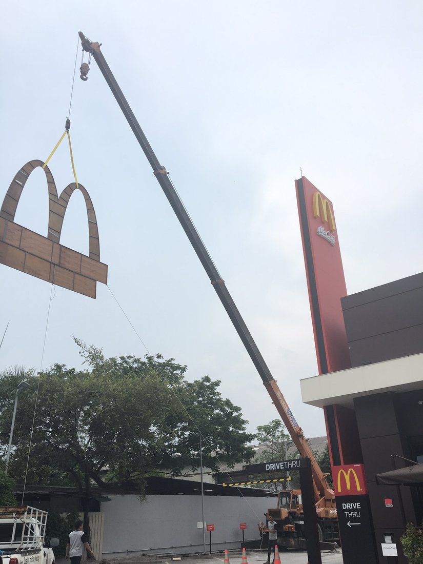 เครนของ BIG MACHINE TRADING ยกป้ายโค้ง M ไม้ขนาดใหญ่ขึ้นติดตั้งที่หน้าร้าน McDonald's ไดรฟ์ทรู
