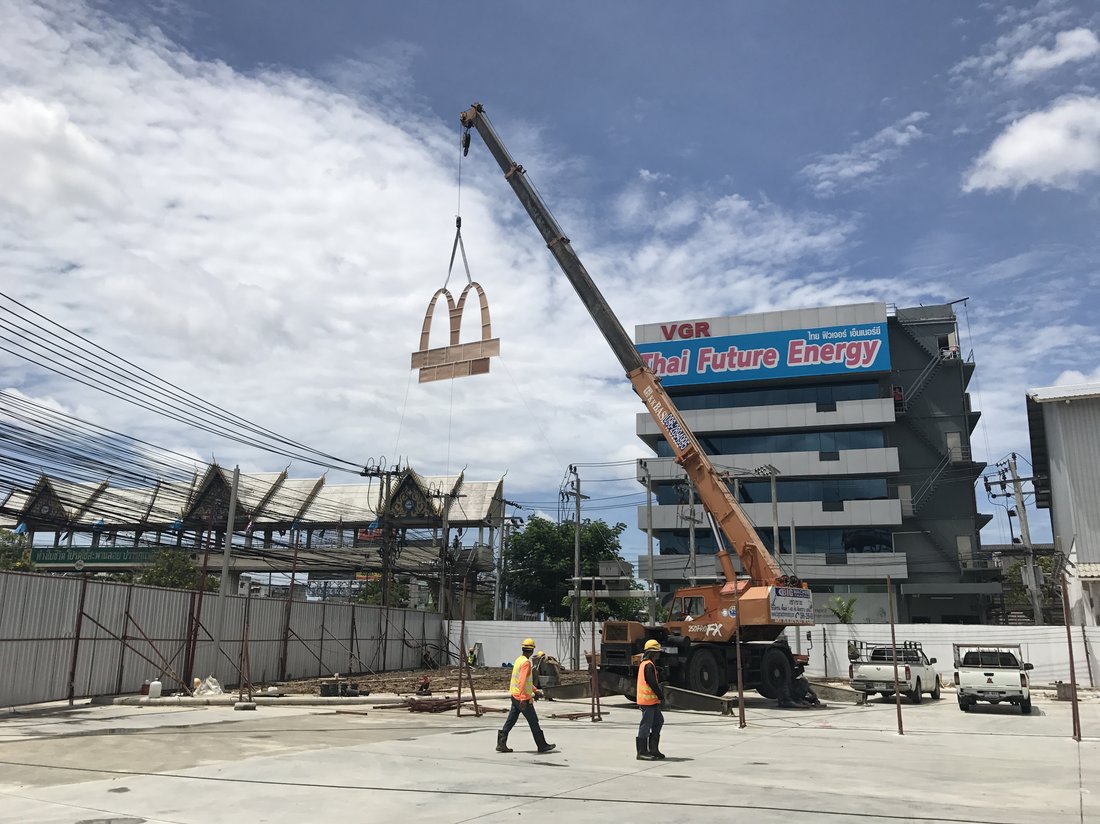 เครนล้อยาง 25 ตัน BIG MACHINE TRADING ยกป้าย McDonald's ขึ้นเสาป้ายในพื้นที่ก่อสร้าง มีทีมงานสวมเสื้อสะท้อนแสงดูแลหน้างาน