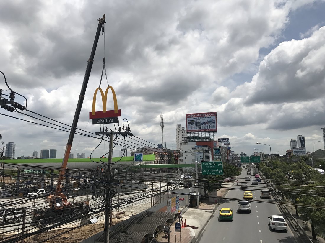 เครนยกป้ายโค้ง McDonald's สีทองขึ้นติดตั้งบนเสาป้ายไดรฟ์ทรู ริมถนนที่มีรถสัญจร
