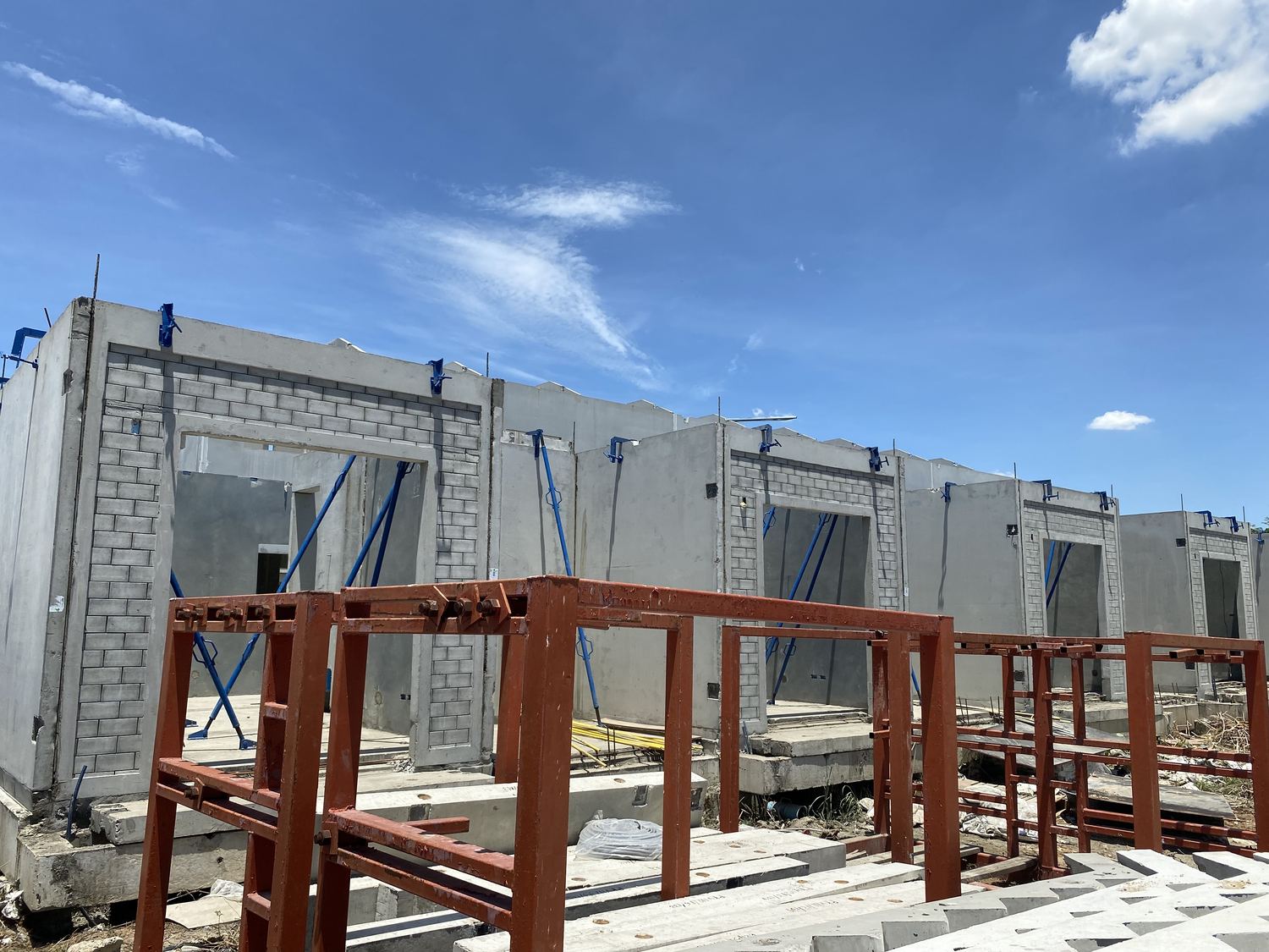 แผ่นคอนกรีตเสริมเหล็กสำเร็จรูป (Precast Panel) ประกอบเป็นผนังบ้าน พร้อมค้ำยันเหล็กชั่วคราว หน้างานหมู่บ้าน