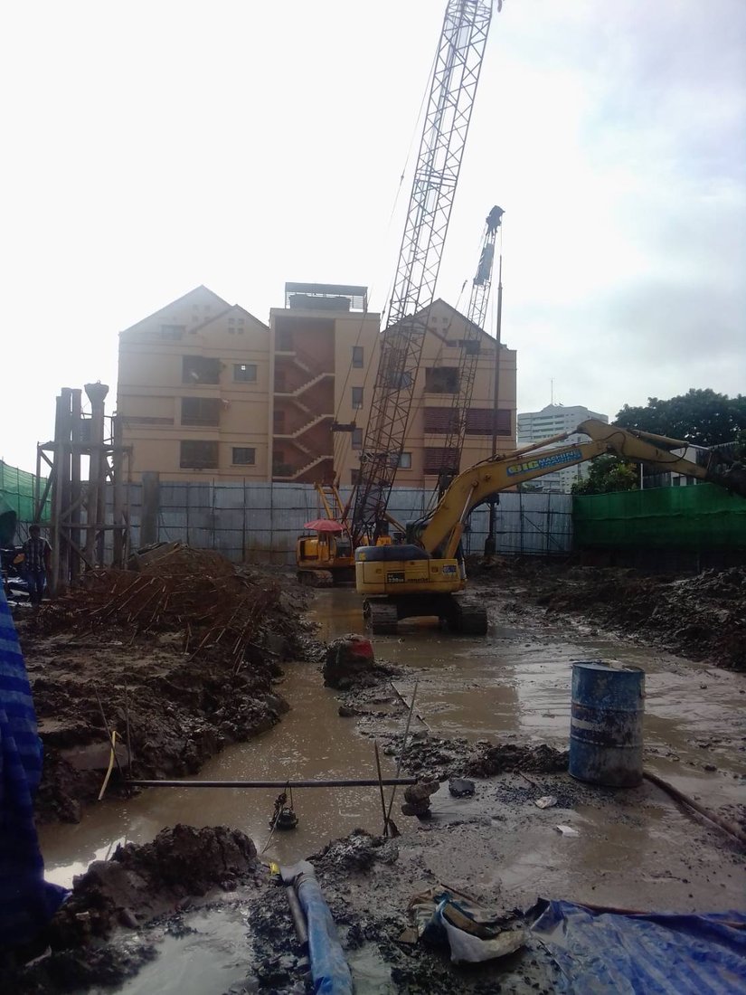 เครนตีนตะขาบ BIG MACHINE TRADING และรถขุด Komatsu ทำงานร่วมกันที่ไซต์เข็มเจาะอาคารพักแพทย์รามาธิบดี เห็นอาคารที่พักอาศัยด้านหลัง
