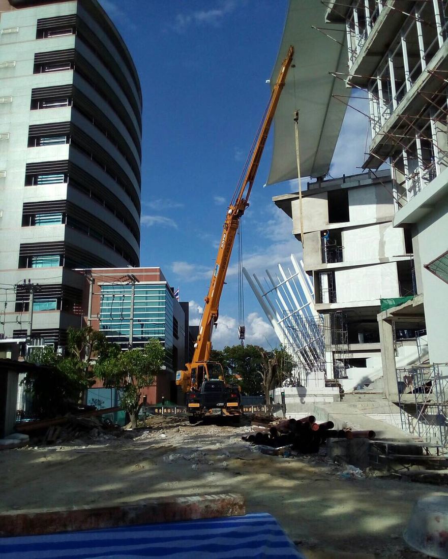 เครนล้อยาง BIG MACHINE TRADING ทำงานระหว่างอาคารมหาวิทยาลัยรังสิต มองเห็นศาลาทรงไทยสีทองด้านหลัง