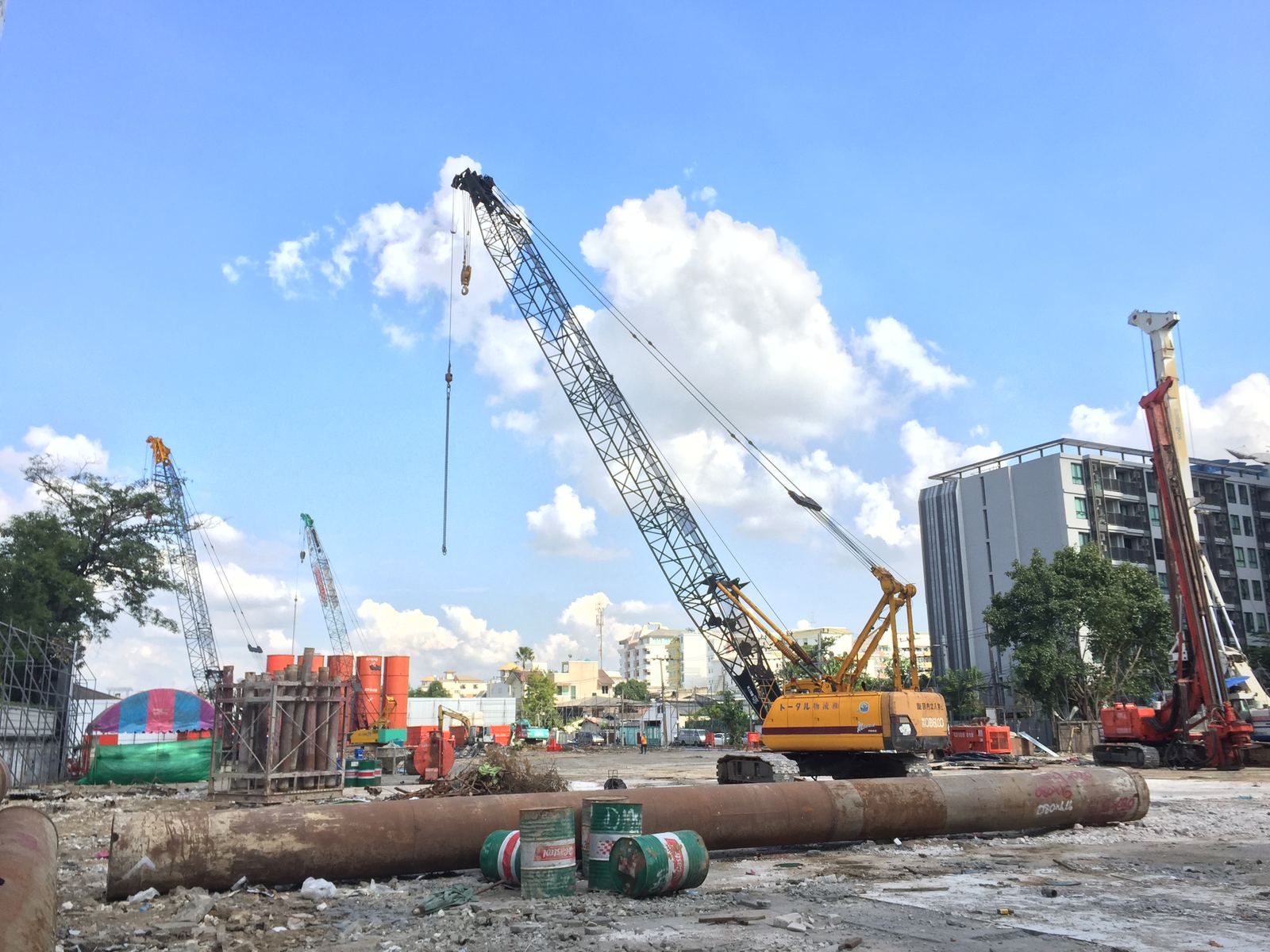 เครนตีนตะขาบเหลือง KOBELCO ทำงานเข็มเจาะเปียก หน้างานคอนโดกรุงเทพฯ ท้องฟ้าแจ่มใส