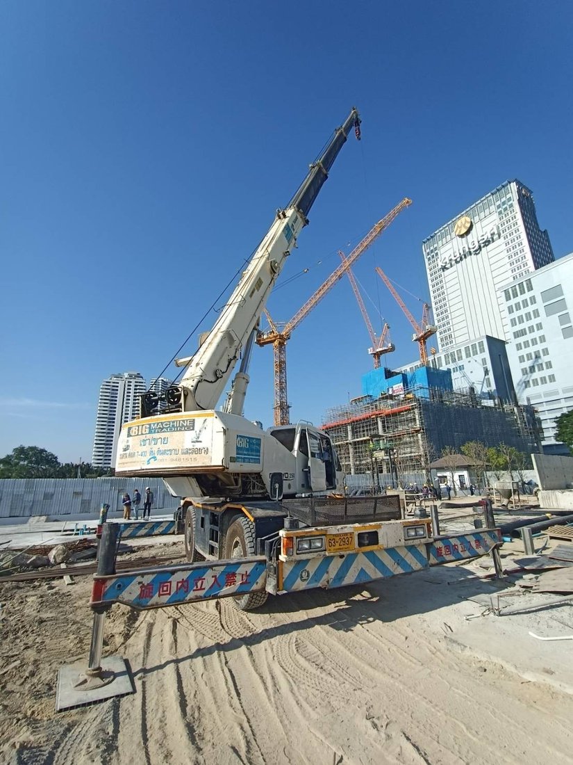 เครนล้อยาง BIG MACHINE TRADING ตั้งขาค้ำยันพร้อมทำงานที่ไซต์ก่อสร้างศุภาลัย ริวา แกรนด์ เห็นป้ายธนาคารกรุงศรีอยุธยาและทาวเวอร์เครนด้านหลัง