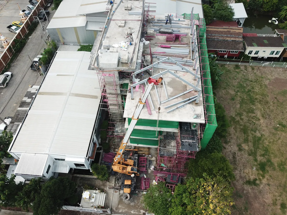 มุมสูงจากโดรน เครน BIG MACHINE TRADING ทำงานยกโครงเหล็กบนดาดฟ้าอาคารในกรุงเทพฯ