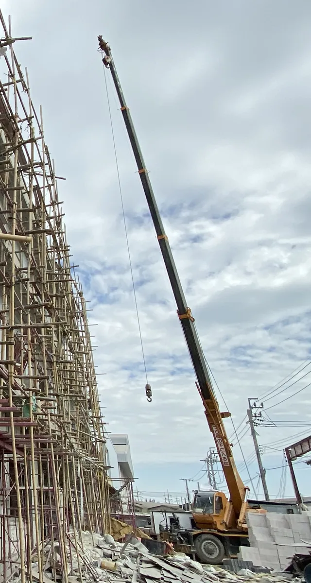 เครน BIG MACHINE TRADING ทำงานข้างอาคารนั่งร้านไม้ไผ่ในสมุทรปราการ เห็นตัวรถ