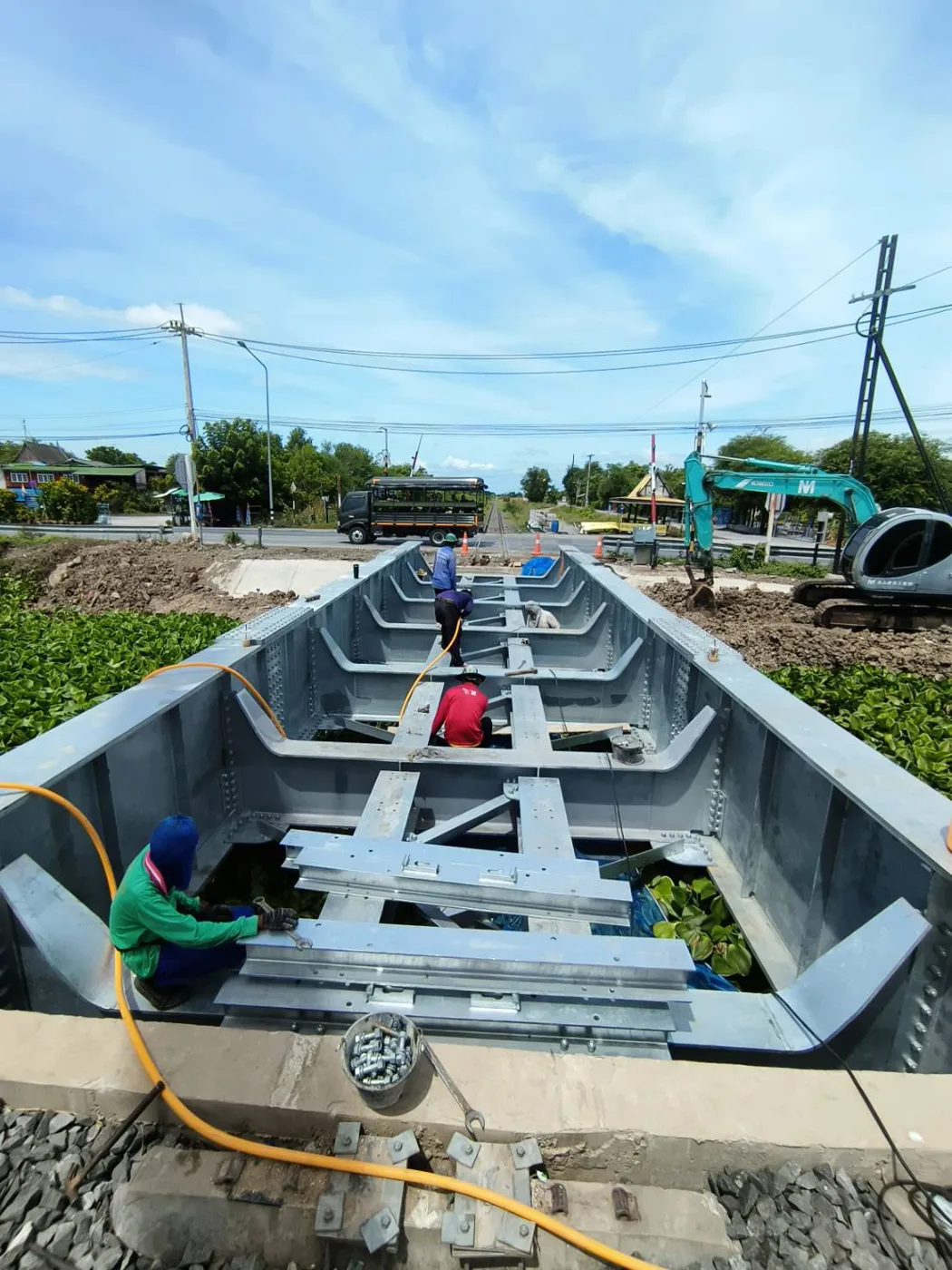 ทีมงานประกอบโครงเหล็กสะพานใกล้จุดตัดทางรถไฟในชุมชน